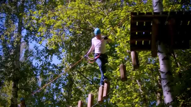 森の木々の間に吊るされた丸太の上を歩く男 — ストック動画