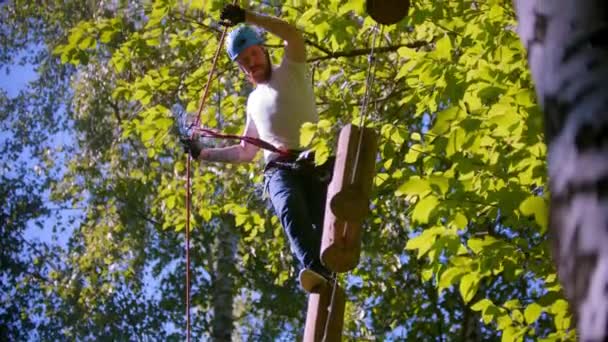 Een man loopt voorzichtig op boomstammen die in de lucht hangen tussen bomen in het bos. — Stockvideo