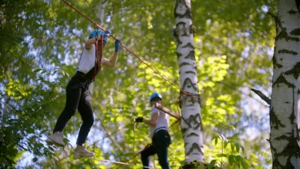 Een vrouw loopt voorzichtig op het touw hangend in de lucht tussen de bomen in het bos - een man wacht tot ze klaar is — Stockvideo