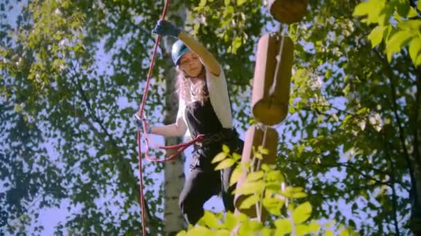 Een vrouw loopt op boomstammen opgehangen in de lucht tussen bomen in het bos - extreem touw avontuur — Stockvideo