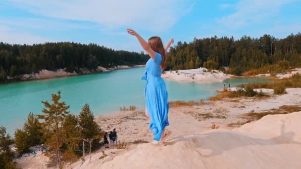 Mujer joven en vestido azul de pie en la playa y tener un momento - el paisaje de lago azul y bosque — Vídeos de Stock