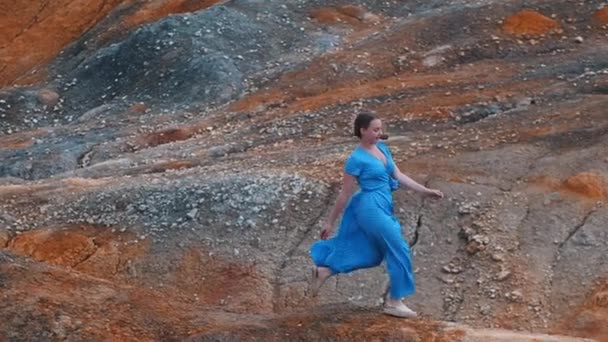 Mujer joven en vestido azul corriendo en una montaña de arcilla naranja y teniendo un momento — Vídeo de stock