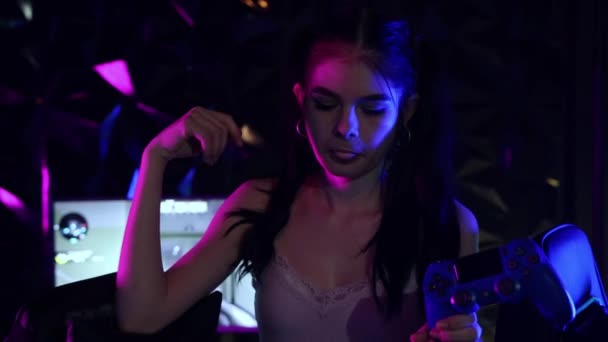 Ung kvinna håller en joystick i neon spelklubb och blåser ett tuggummi - skrattar — Stockvideo