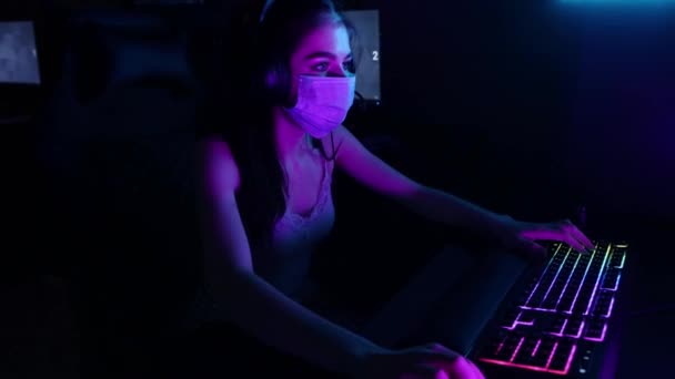 Jonge vrouw in hoofdtelefoon en een gezichtsmasker spelen van een online spel in gaming club — Stockvideo