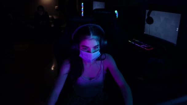 Jeune femme en casque et masque blanc jouant à un jeu en ligne dans le club de jeu — Video