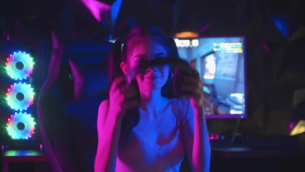 Ung kvinna spelar ett online-spel i gaming club - sätta på sina hörlurar och vänder sig till skärmen — Stockvideo