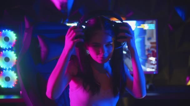조랑말 꼬리를 가진 젊은 여성이 게임 클럽에서 게임을 하는 모습 - 헤드폰을 쓰고 모니터를 켜는 모습 — 비디오