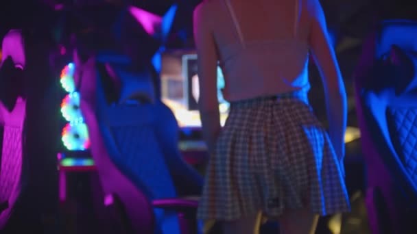 Mujer joven en falda camina a una computadora en el club de juego y se sienta en la silla — Vídeo de stock