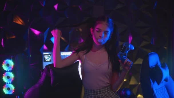 Młoda seksowna kobieta z kucykiem trzymająca joysticka w klubie gier neonowych i dmuchająca gumę do żucia — Wideo stockowe