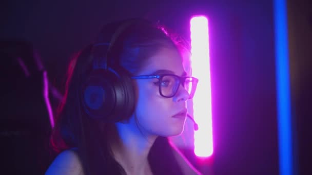 Mujer bonita joven en gafas jugando juegos en línea en el club de juegos de neón — Vídeos de Stock