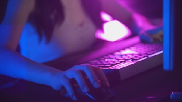 Молодая женщина в очках играет в онлайн-игры в неоновом игровом клубе - мышь и освещаемая клавиатура — стоковое видео