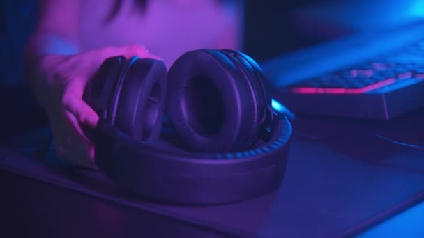 Νεαρή γυναίκα που κάθεται στο νέον gaming club και φοράει μεγάλα ακουστικά - κοιτάζοντας στην κάμερα — Αρχείο Βίντεο