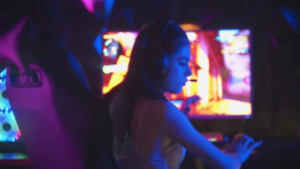 Mujer bonita joven sentada en el club de juego de neón y jugar juegos - se aleja del monitor y mirando a la cámara — Vídeo de stock