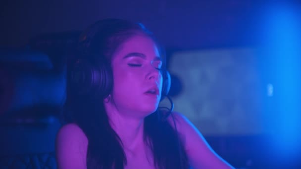 Junge attraktive Frau mit leichtem Make-up sitzt im neonfarbenen Spielclub - trauriges Seufzen und hält ihren Kopf — Stockvideo