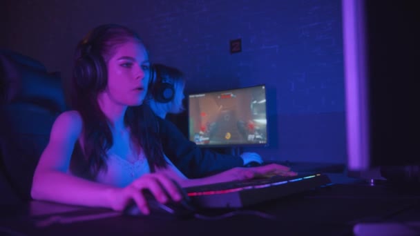 Две симпатичные девушки-геймеры играют в онлайн-шутер в клубе темных неоновых игр — стоковое видео