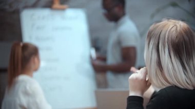 Sınıfta siyahi bir öğretmenle İngilizce dersi. Masada oturan iki kadın. Biri elini kaldırıyor.