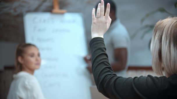 Cours d'anglais dans la classe avec un professeur noir - deux femmes assises à la table et l'une d'elles lève la main et sort de la classe — Video