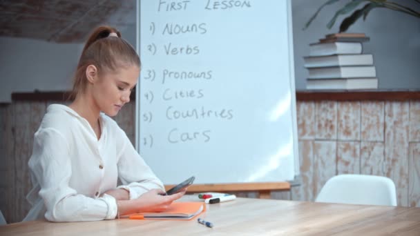 Jeune femme blonde assise en classe d'anglais et utilisant son téléphone — Video