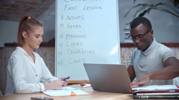 Vrouw en Afrikaans-Amerikaanse man wachtend op hun leraar in de Engelse les - kijkend naar het bestuur — Stockvideo