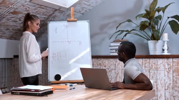 Een algebra les - vrouw die bij het bord staat met grafieken van functies en een zwarte man die aan tafel zit — Stockvideo