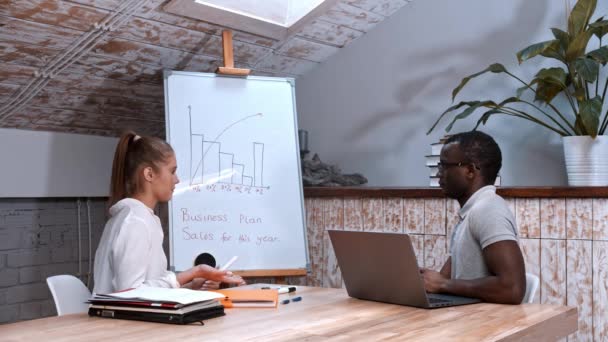 Hombre afroamericano y mujer caucásica en la reunión de negocios - señalando a la junta con gráficos — Vídeos de Stock