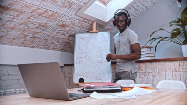 Une leçon de mathématiques en ligne - un enseignant afro-américain debout près du tableau et explique le matériel pour ses élèves devant l'ordinateur portable — Video