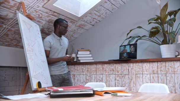 Une leçon de mathématiques en ligne - un enseignant afro-américain dans des lunettes debout près du tableau et explique le matériel pour ses élèves à l "écran — Video