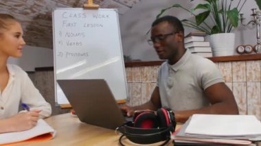 İngilizce sınıfı - bir kadın ve Afrika kökenli Amerikalı bir erkek - bir adam dizüstü bilgisayarın başında oturuyor ve gülüyor ve bir kadın notlar alıyor