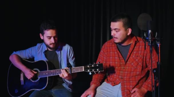 Двое мужчин записывают песню в студии звукозаписи - играют на гитаре и поют — стоковое видео