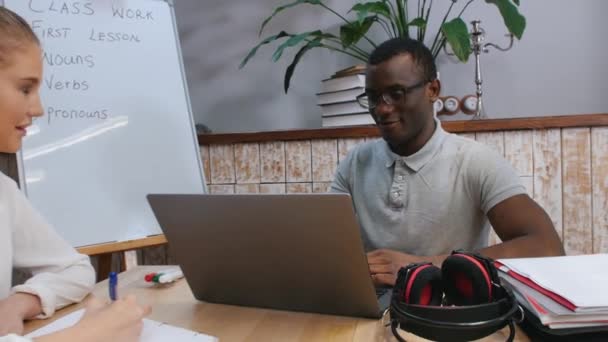 Τάξη αγγλικών - μια γυναίκα και ένας Αφροαμερικάνος που έχουν μάθημα αγγλικών - ένας άντρας που κάθεται δίπλα στο laptop — Αρχείο Βίντεο