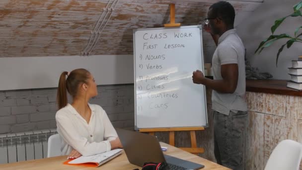 Um homem afro-americano que dá uma lição de inglês a uma mulher no escritório moderno — Vídeo de Stock