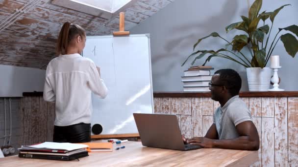 Une leçon dans la classe - une femme écrivant sur le tableau et un homme noir assis à la table — Video