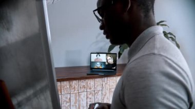 Çevrimiçi bir ders. Gözlüklü Afro-Amerikan bir erkek öğretmen tahtada duruyor ve öğrencilerine bilgisayar ekranındaki materyalleri anlatıyor.