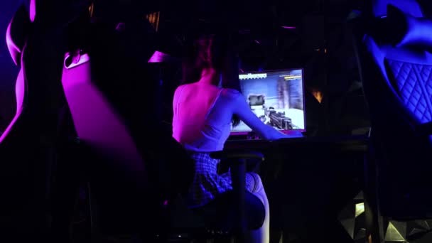 한 젊은 여자가 게임 클럽에서 의자에 앉아 슈팅 게임을 하고 있습니다 - 돌아서 카메라를 보면서 — 비디오