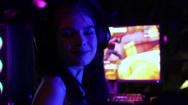 Mladá hezká žena sedí v křesle v herním klubu a hraje střílečku - usmívá se do kamery — Stock video