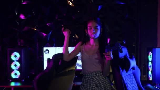 Jovem mulher sexy segurando um joystick no clube de jogos e sopra uma pastilha elástica — Vídeo de Stock