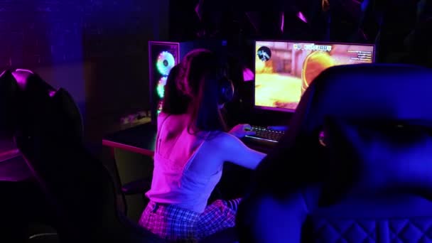 Ung kvinna i hörlurar spelar ett online-spel i neon gaming club — Stockvideo