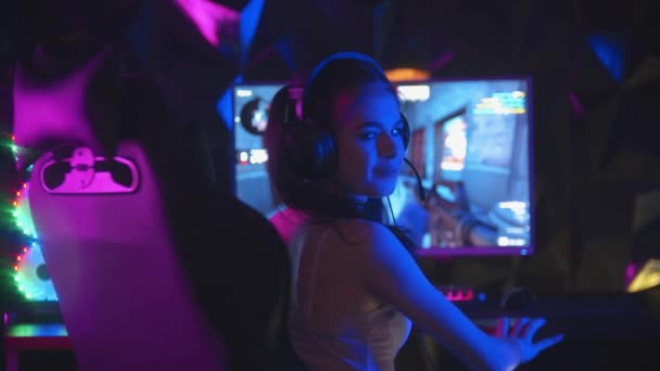 Mujer joven jugando un juego en línea en el club de juego - se quita los auriculares y se gira hacia la cámara — Vídeos de Stock