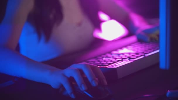 Neon oyun kulübünde gözlüklü genç bir kadın online oyunlar oynuyor - fare ve klavye aydınlığı — Stok video