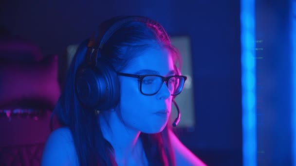 Ung söt kvinna i glasögon spelar online-spel i modern neon gaming club - bär hörlurar och talar i mikrofonen — Stockvideo