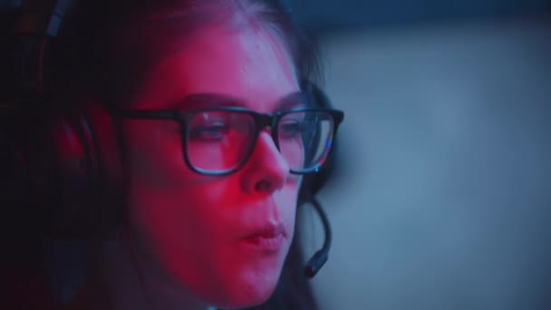 Gözlüklü çekici bir kadın modern neon oyun kulübünde oyun oynuyor ve sakız çiğniyor. — Stok video