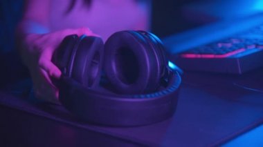 Genç bir kadın neon oyun kulübünde oturuyor ve büyük kulaklıklar takıyor. Kameraya bakıyor.