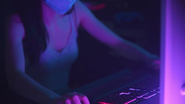 Wanita muda dengan headphone dan topeng wajah pelindung putih memainkan game online di klub game — Stok Video