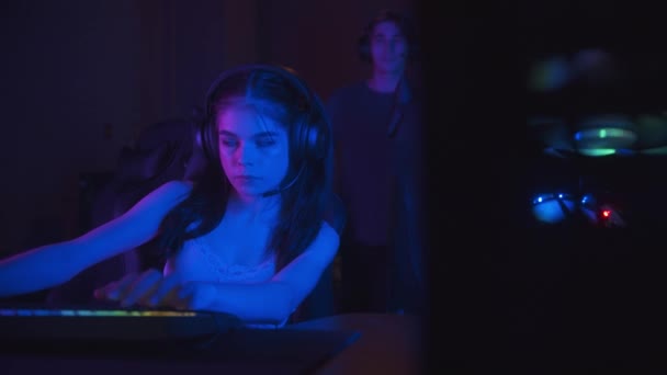 Dos chicas jugando un juego en línea en el club de juegos de neón - su amigo viene a ellos y comienza a hablar — Vídeos de Stock
