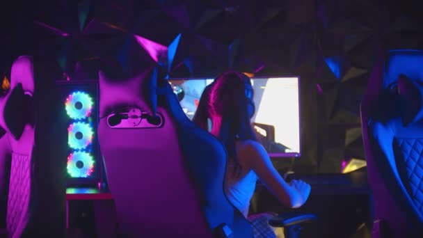 Wanita cantik duduk di klub game neon dan bermain game-berpaling dari monitor, mengambil headphone dan melihat ke kamera — Stok Video