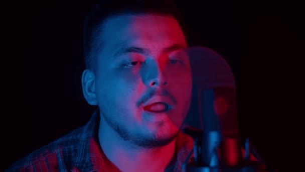 Concept de musiciens - homme assis dans un studio sombre en lumière rouge et bleue et chantant une chanson au microphone — Video
