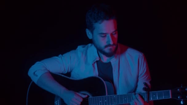 Человек, играющий на гитаре в темной студии — стоковое видео