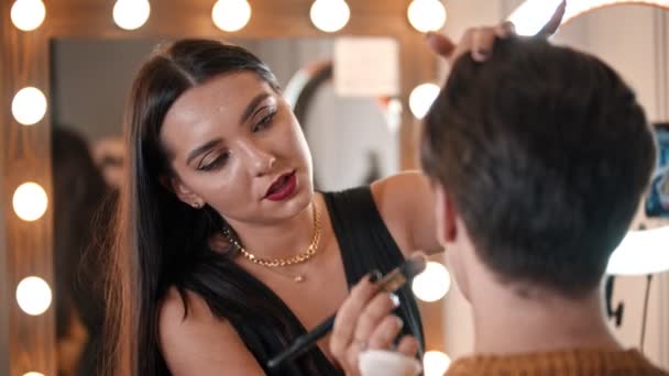 Make-up-Künstlerin trägt mit Pinsel Basis auf das Gesicht des männlichen Models auf — Stockvideo