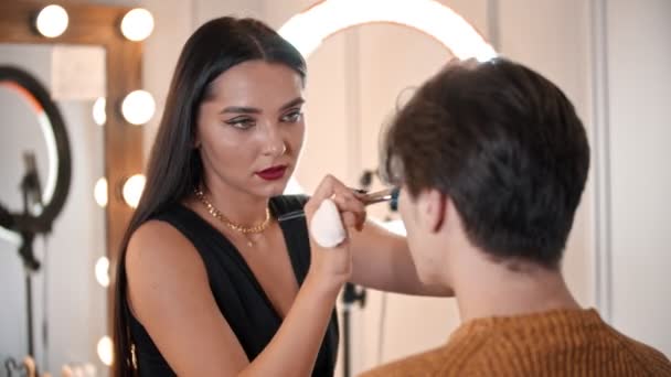 Preciosa mujer maquillaje artista aplicando la fundación en la cara de modelo masculino utilizando un cepillo — Vídeos de Stock