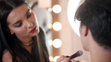 Makyaj sanatçısı erkek modelin yüzüne kabarık bir fırça kullanarak pudra sürüyor.